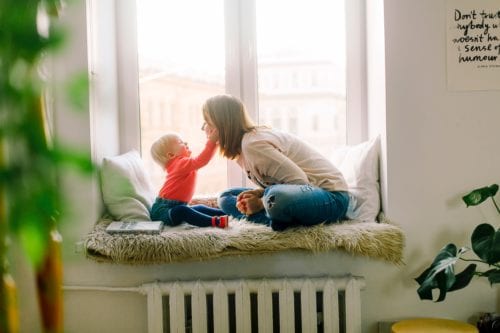 Mother faces her small child while sitting in a window