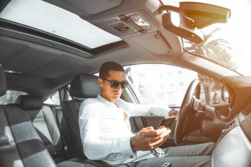 Young man looks at his phone from behind the wheel of a car