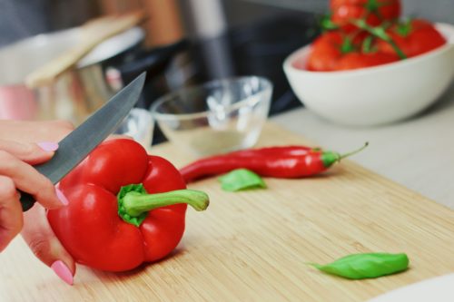 A woman with pnik nails cutting a red bell pepper