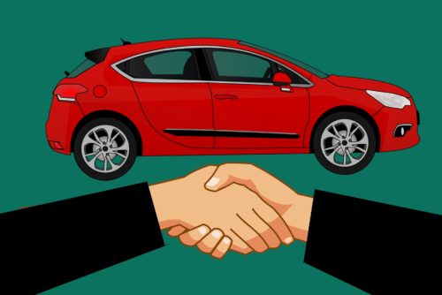 Two people shaking hands in front of a car